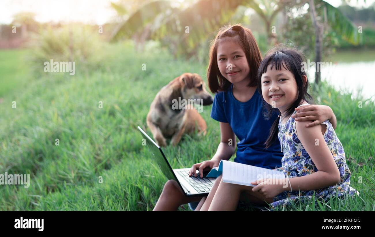 Happy two little child girl learning outdoor by studying online and working on laptop in the green farm field Stock Photo