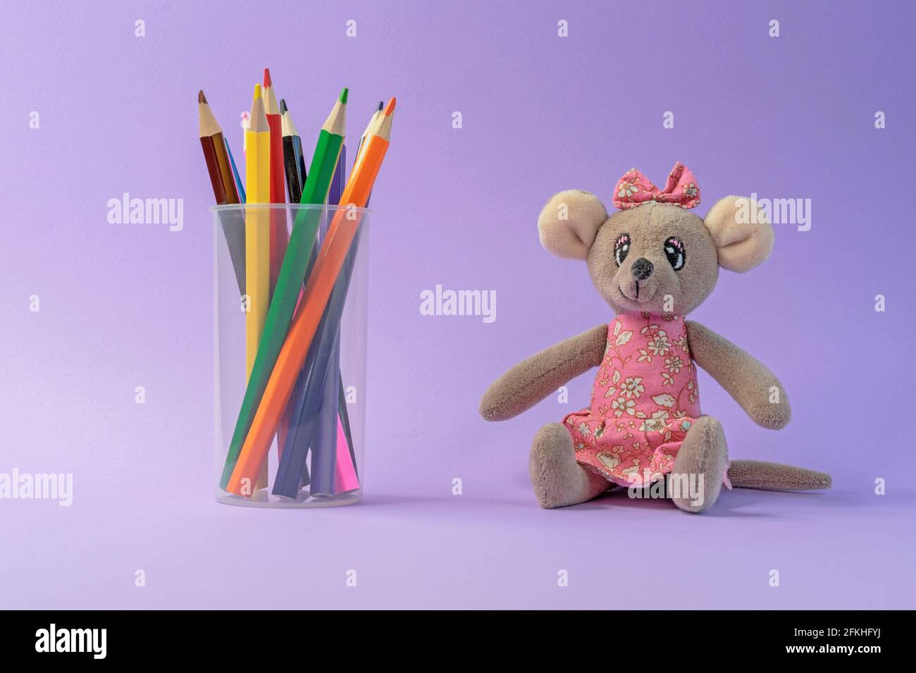 Colored pencils in a plastic cup and a toy mouse on a lilac background. Stock Photo