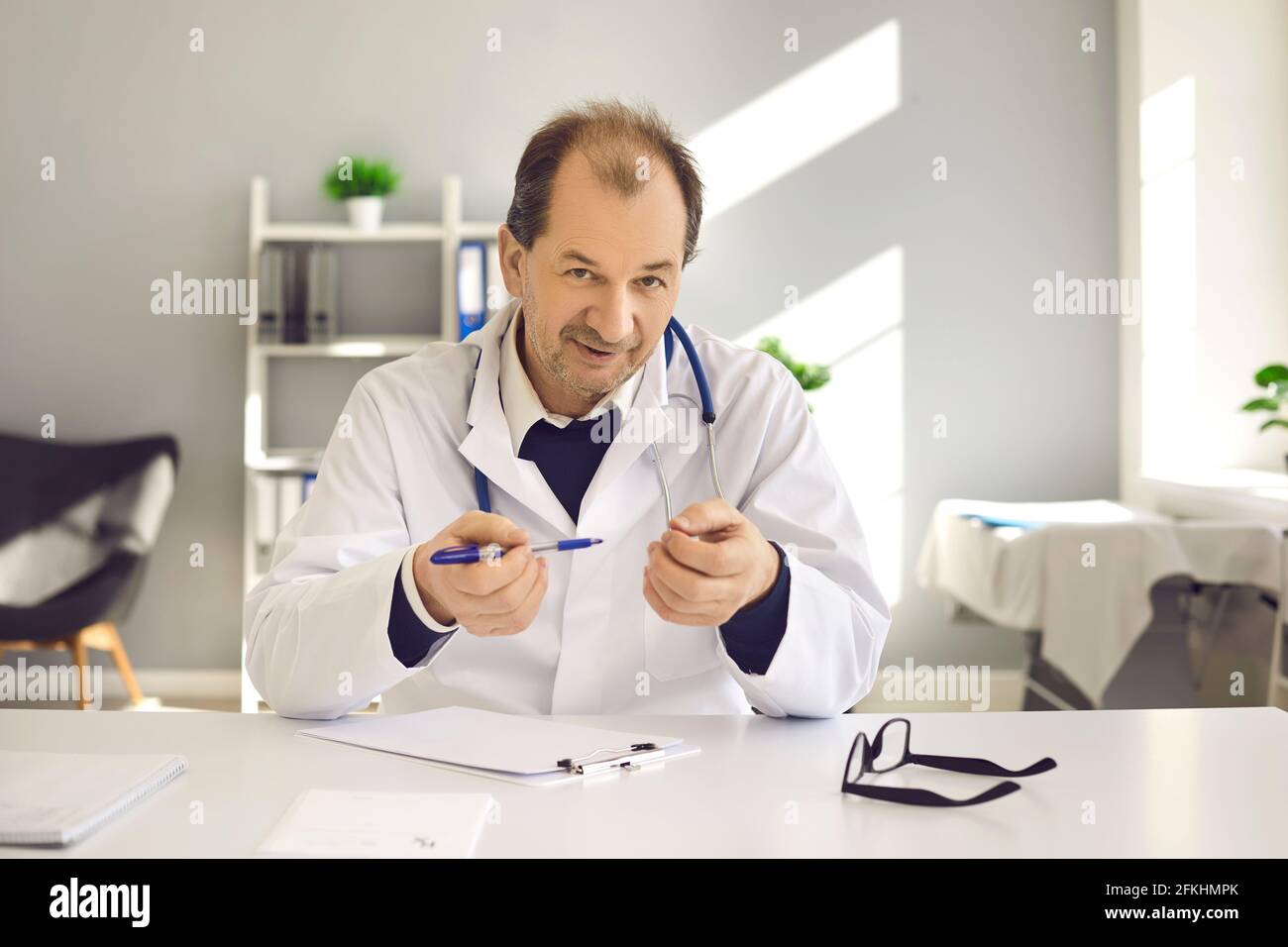 Doctor at desk consulting patient online explaining prescription to camera Stock Photo