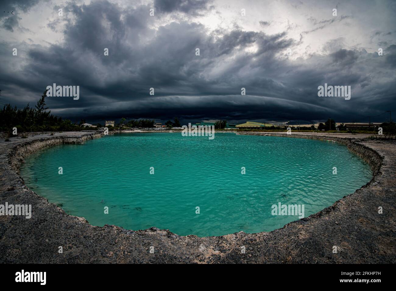 The large black thunderstorm clouds or  Arcus cloud, are above the emerald pond. Stock Photo