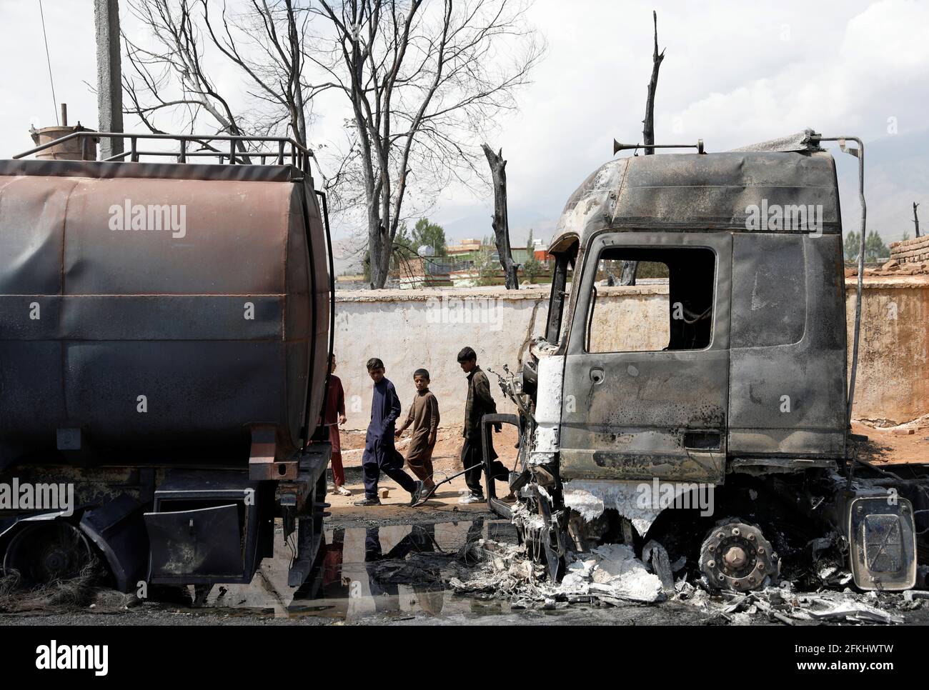 Boys walk past burnt fuel tankers after an overnight fire, on the outskirts of Kabul, Afghanistan May 2, 2021. REUTERS/Mohammad Ismail Stock Photo