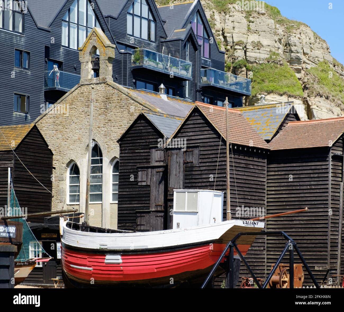 Staycation idea. The Stade Hastings, old fishing boat Valiant, Net Shops & Fisherman’s Museum. Townhouses & Hastings Country Park sandstone cliffs. Stock Photo