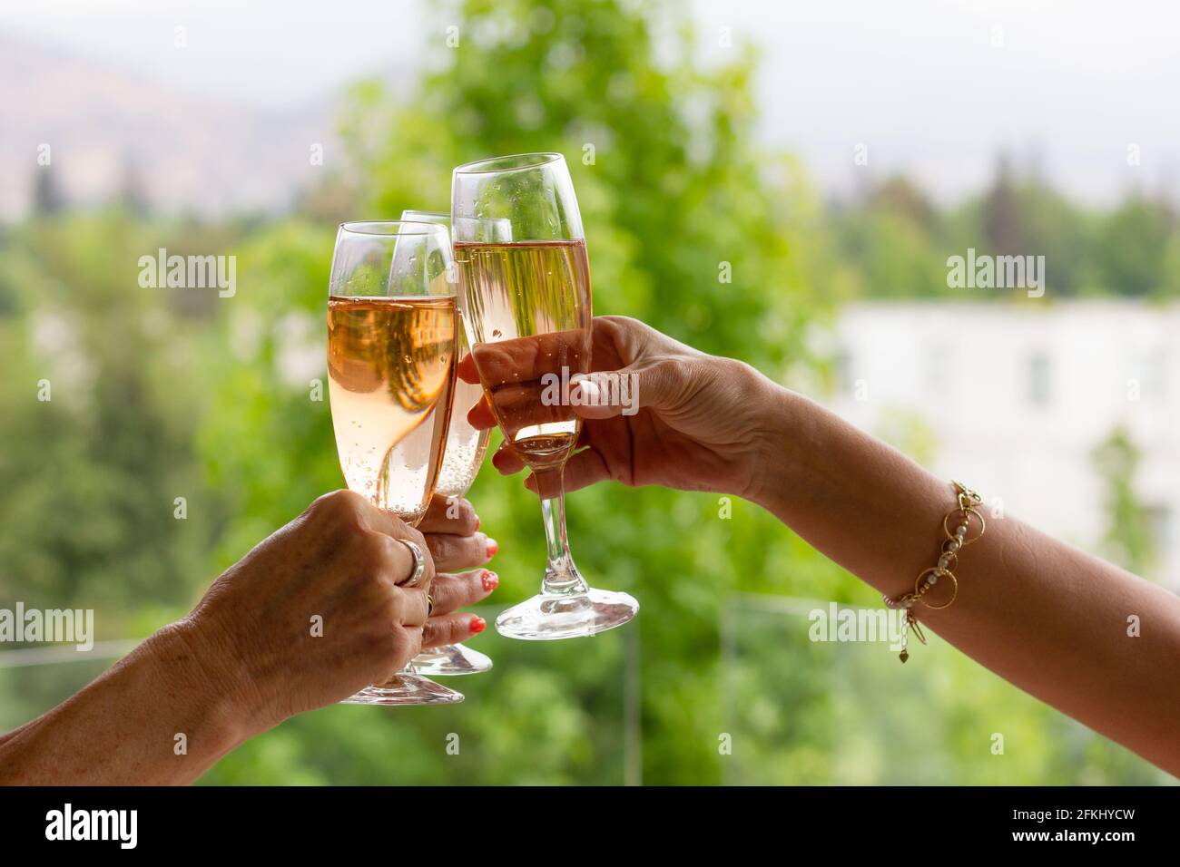 Hands of women raising sparkling rose wine glasses on daytime celebration. Cheers, drink toast party concepts Stock Photo