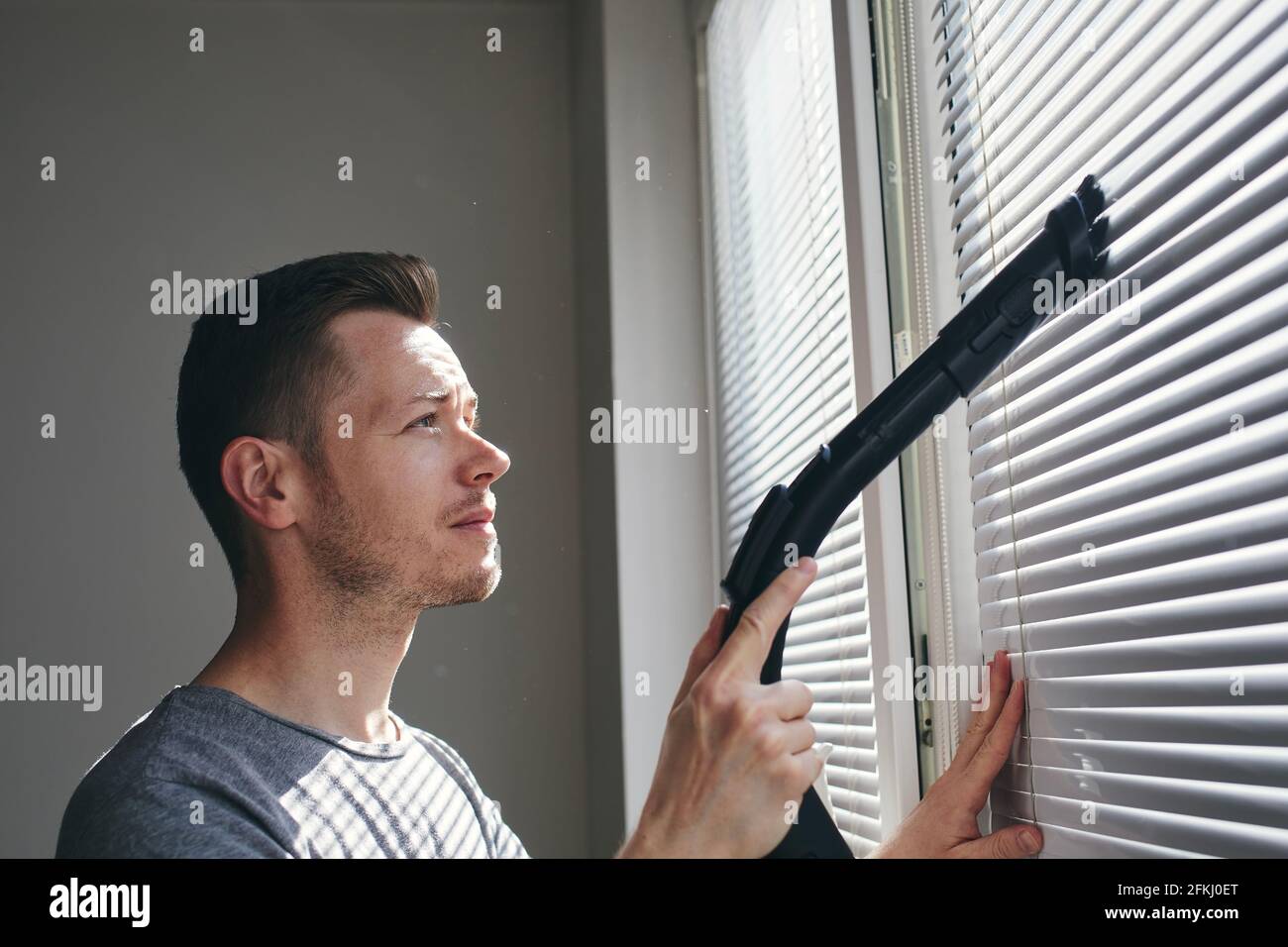 Man cleaning dust from window blind by vacuum cleaner at home. Themes