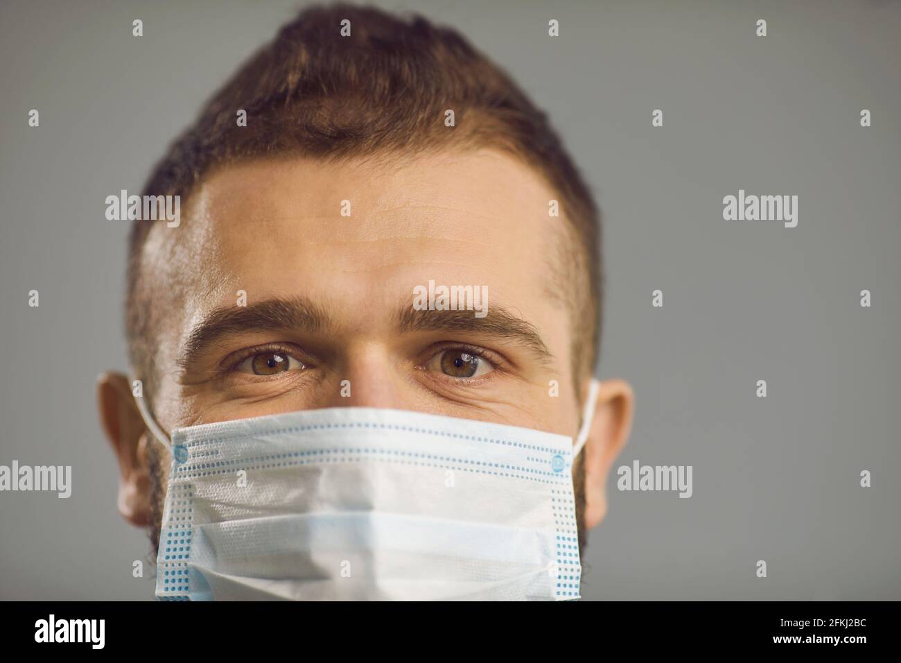 Eyes of a Caucasian millennial guy who is wearing a protective medical mask on a gray background. Stock Photo