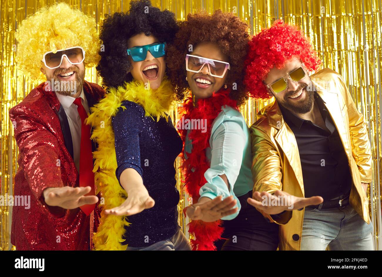 Happy young people in feather boas and curly wigs dancing and having fun at the club Stock Photo
