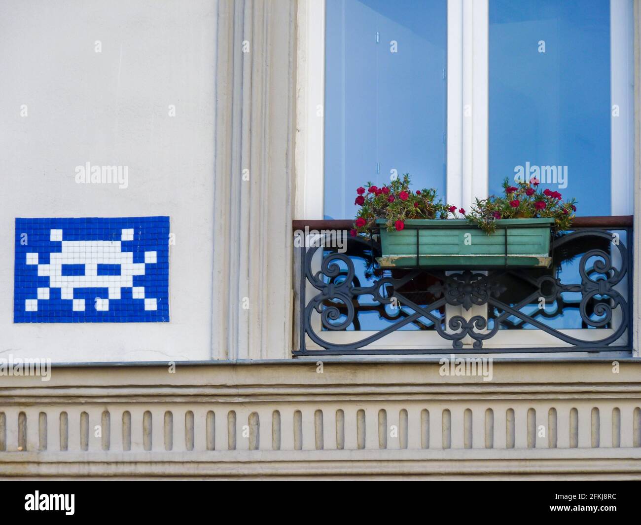 Street art in blue white, work of space invader in Paris on a facade of a historical building with a french balcony and flowers in city center. Stock Photo