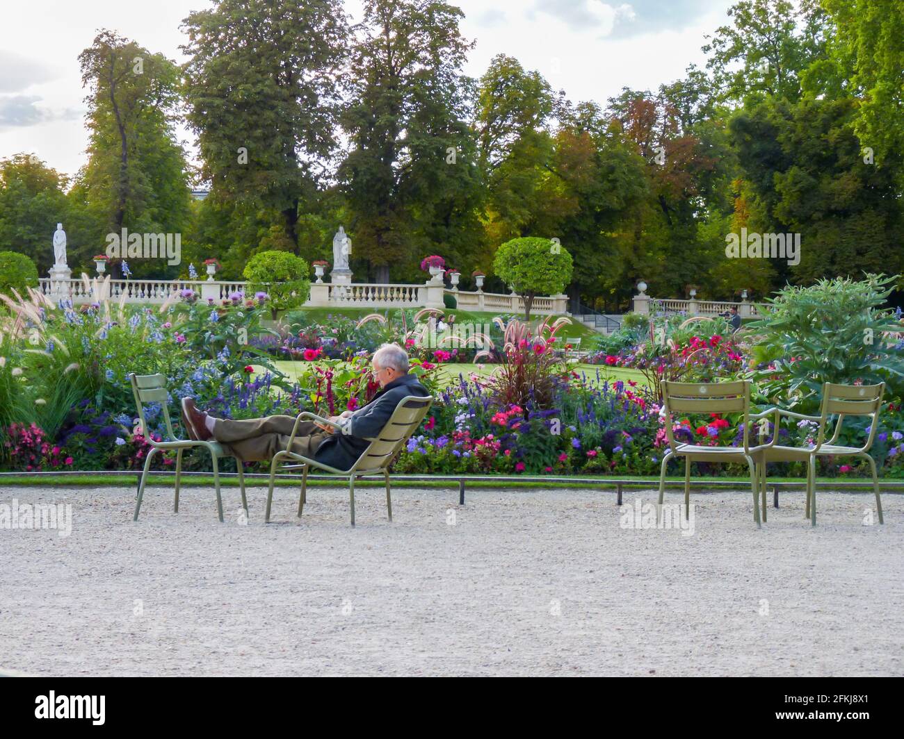 A person having rest on two typical green chairs in Luxembourg Garden, Paris next to flowers in blossom. Stock Photo