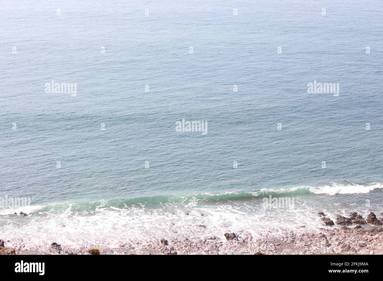 A landscape coastal photograph of the ocean breaking gently against ...