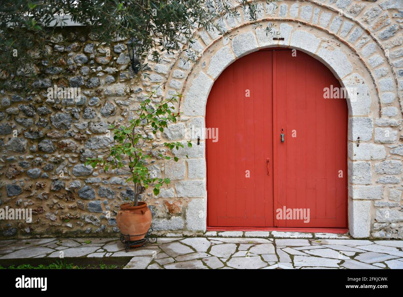 Old rural house facade with a weathered stone wall and a red arched ...