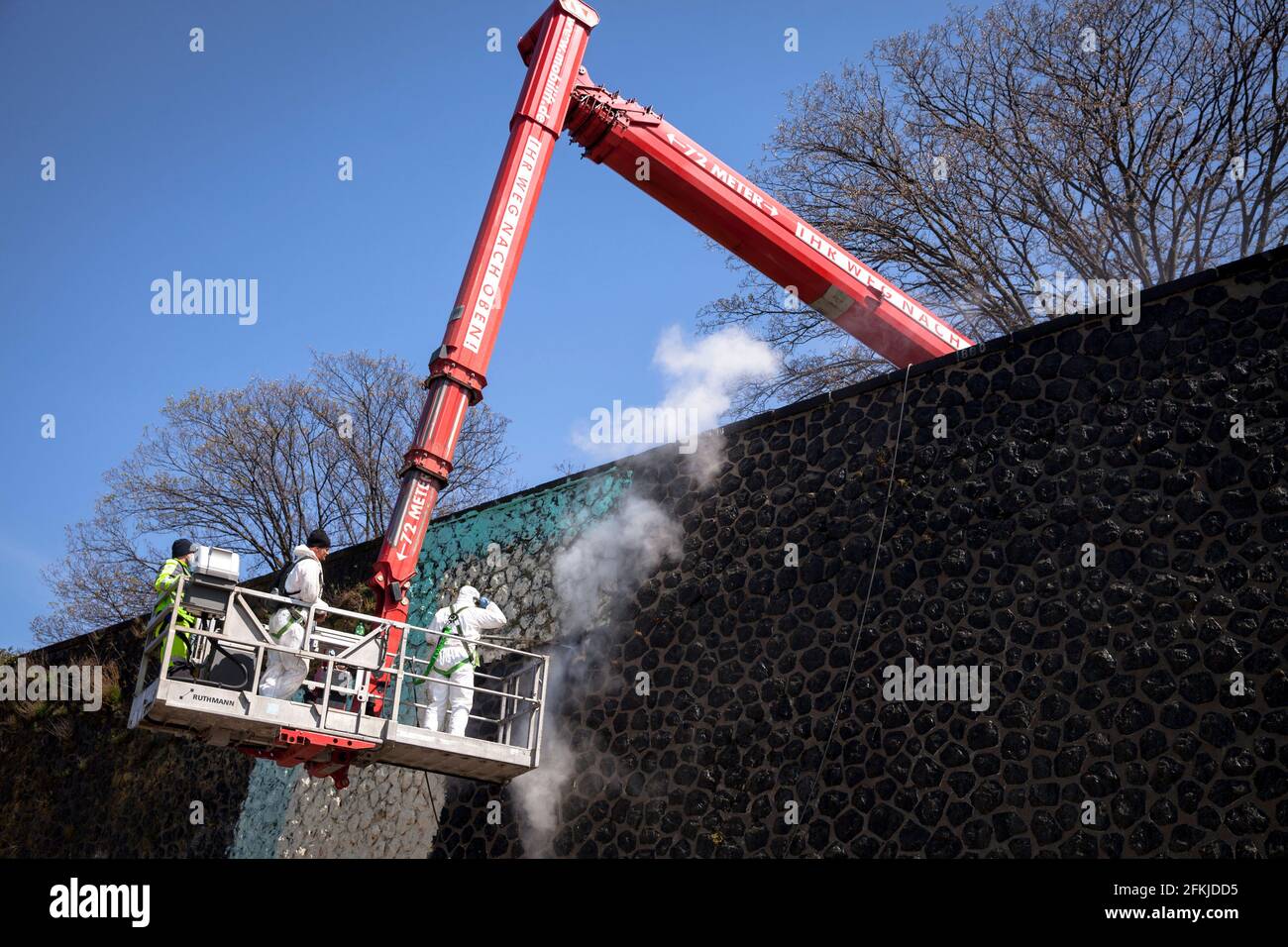 workers on a aerial work platform remove an illegal large graffiti on the bank wall on the river Rhine in Deutz district, Cologne, Germany.  Arbeiter Stock Photo
