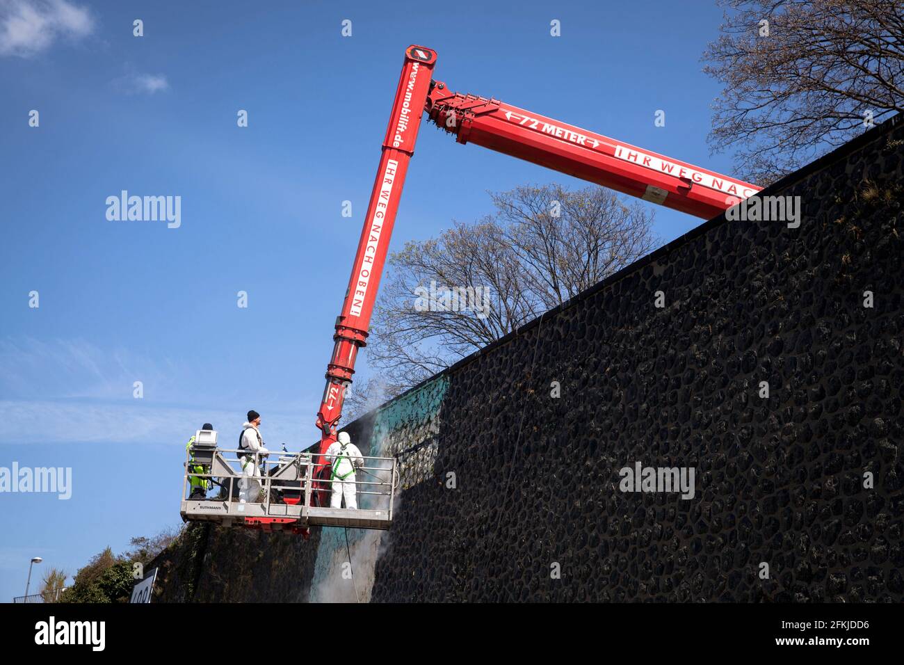 workers on a aerial work platform remove an illegal large graffiti on the bank wall on the river Rhine in Deutz district, Cologne, Germany.  Arbeiter Stock Photo