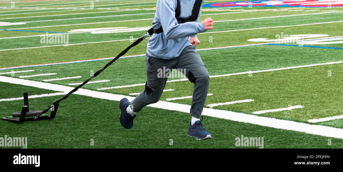 A high school track and field runners is pulling a sled with weights on