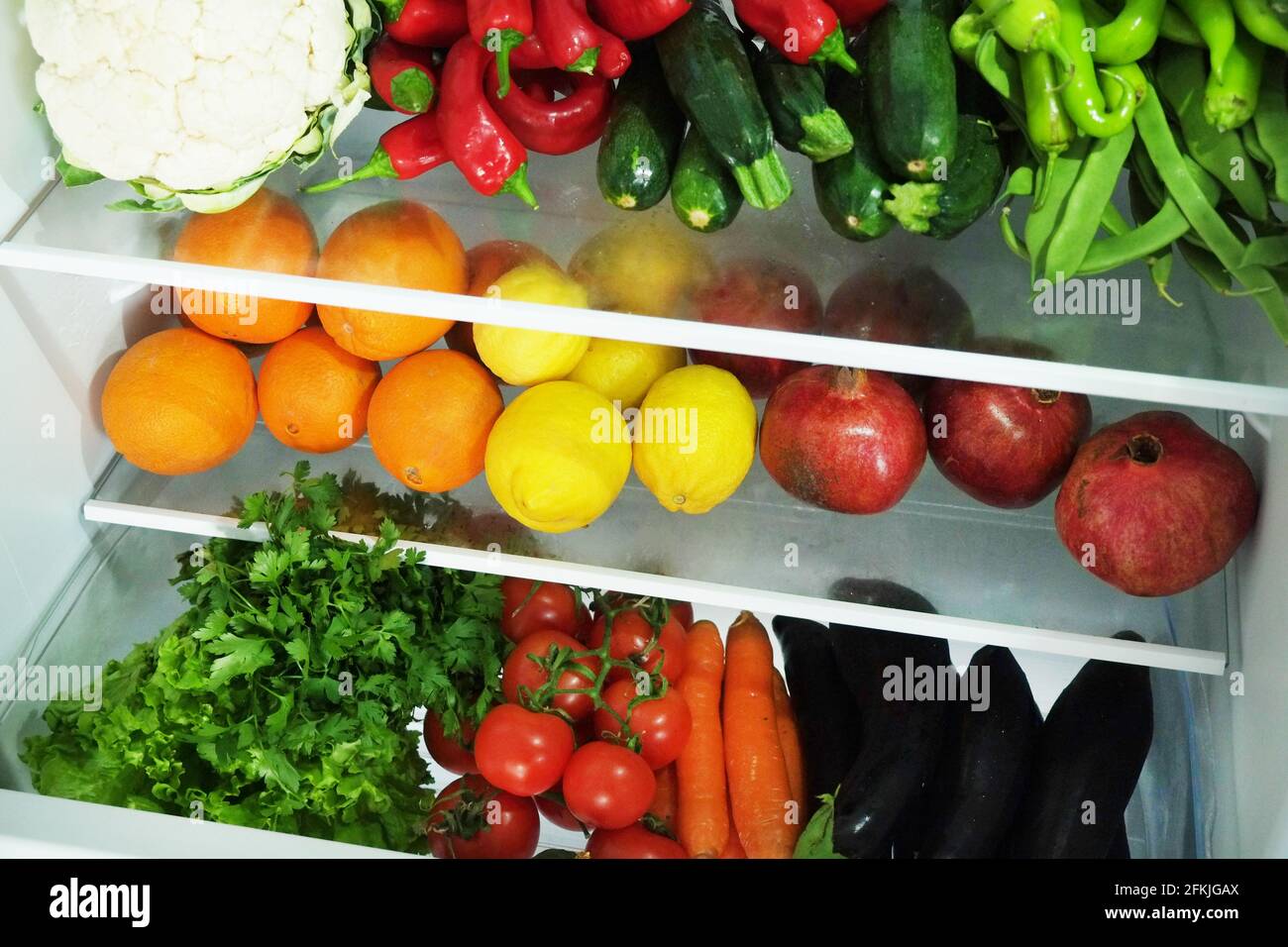 Stacked fridge full of fresh organic fruits and vegetables: orange, lemon, pomegranate, eggplant, carrot, parsley, pepper, cucumber, cauliflower, toma Stock Photo
