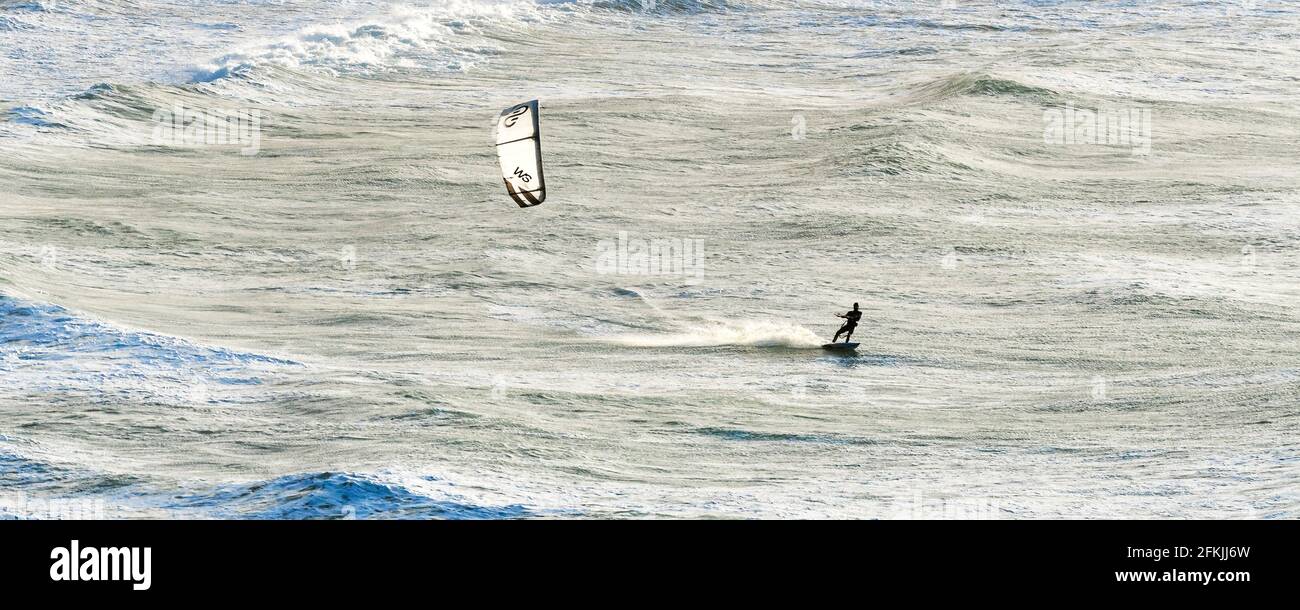 A panoramic image of a kite surfer riding waves in high winds at Crantock beach in Newquay in Cornwall. Stock Photo