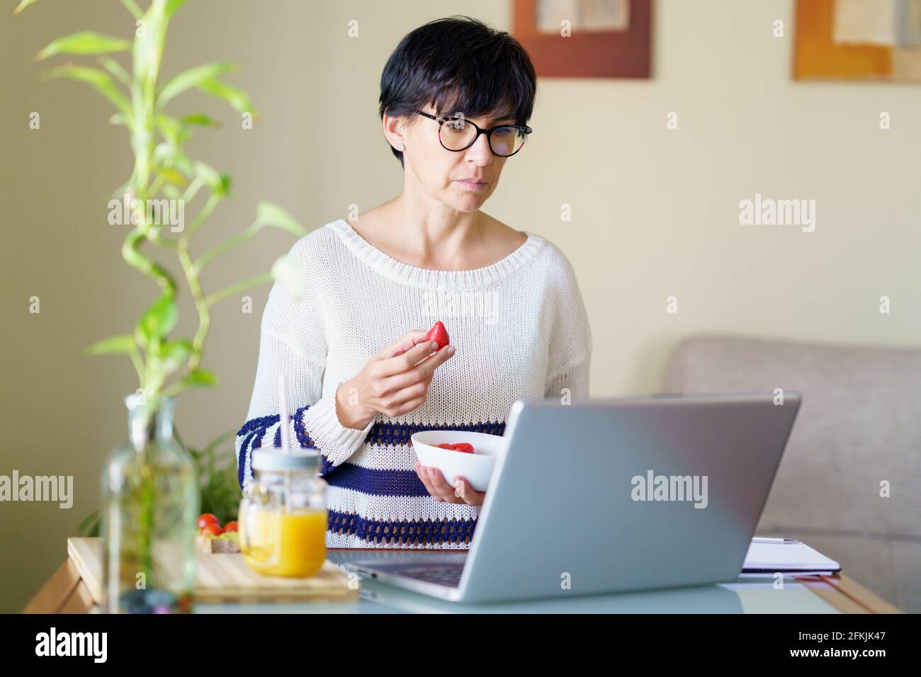 Woman eating strawberries while teleworking from home on her laptop Stock Photo