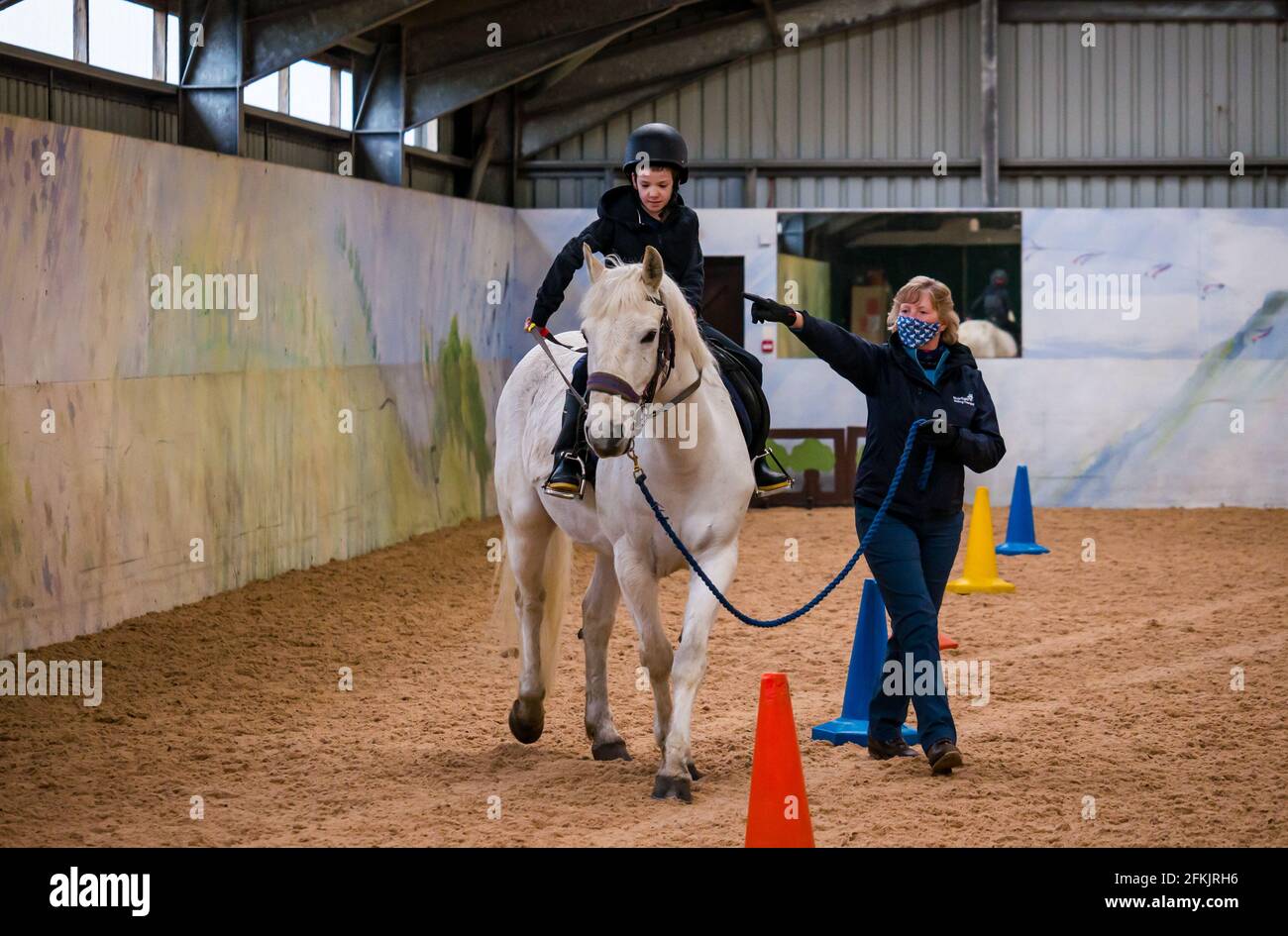 Boy riding white horse learning rein control, Riding for disabled at Muirfield Riding Therapy, East Lothian, Scotland, UK Stock Photo