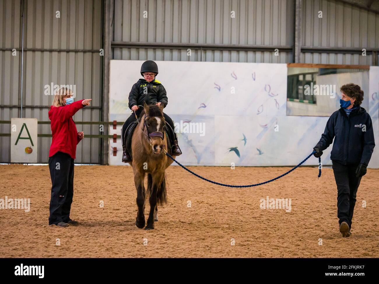 Boy with Down's Syndrome riding horse with coach instructing, Riding for disabled at Muirfield Riding Therapy, East Lothian, Scotland, UK Stock Photo