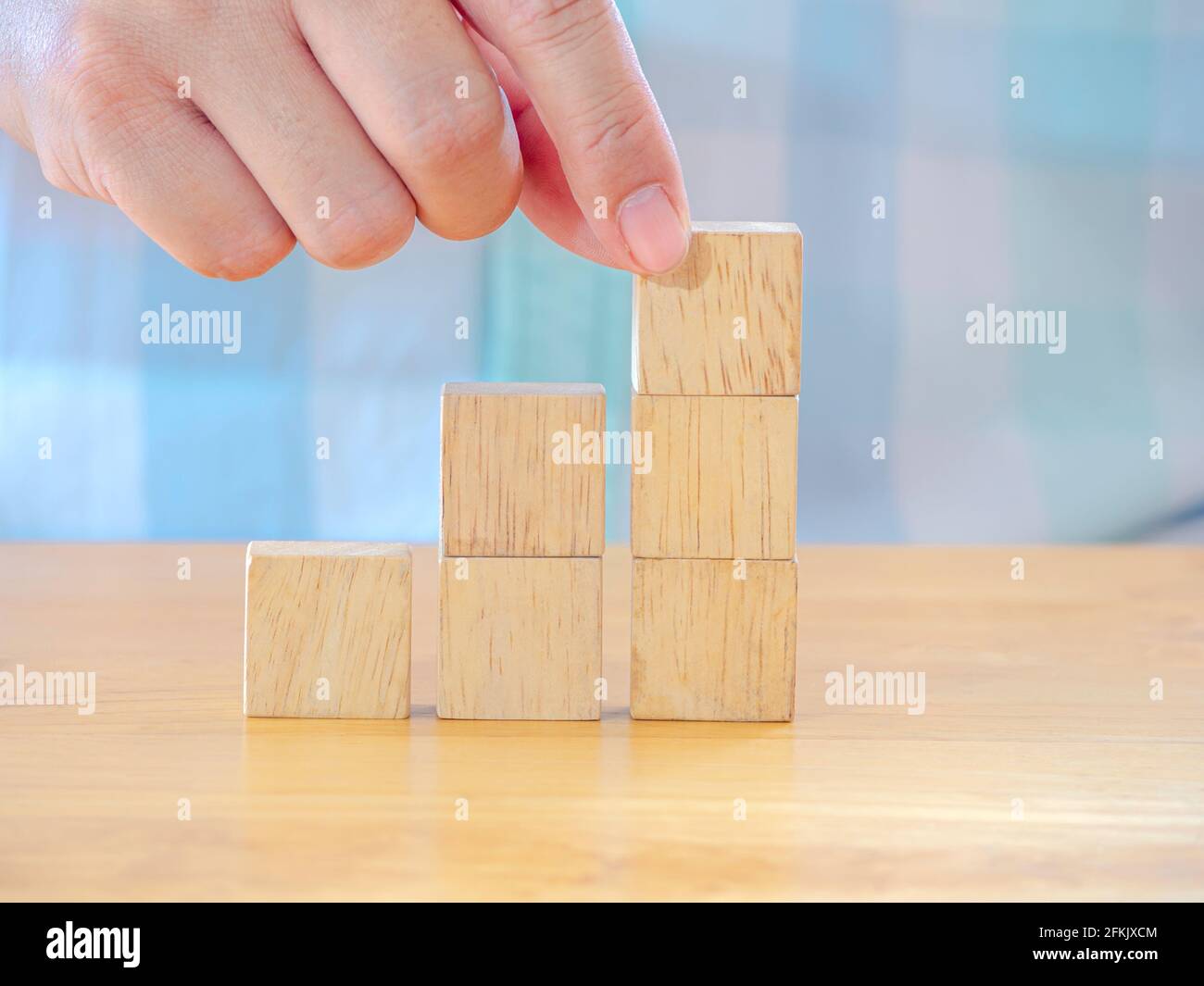 Hand arranging wood cube stacking as stair step shape on wooden table ...