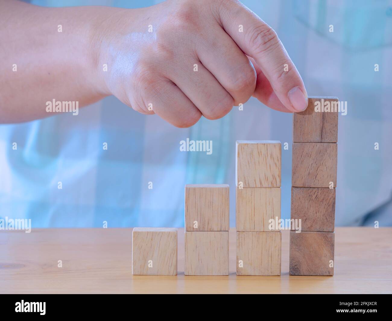 Hand arranging wood cube stacking as stair step shape on wooden table ...