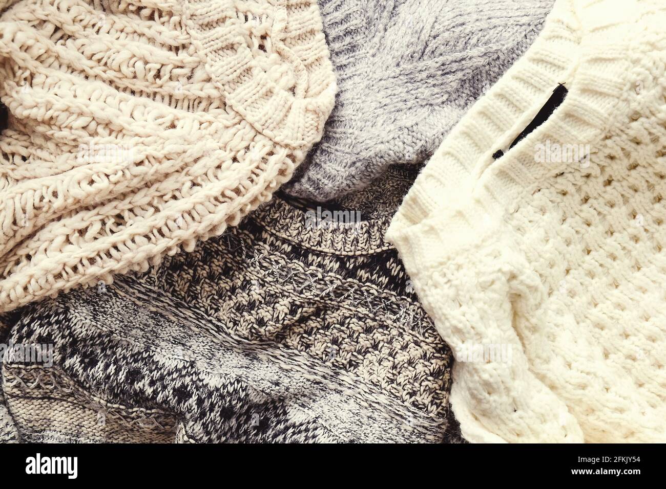 Bunch of knitted warm pastel color sweaters with different knitting patterns laid in messy pile, clearly visible texture. Stylish fall / winter season Stock Photo