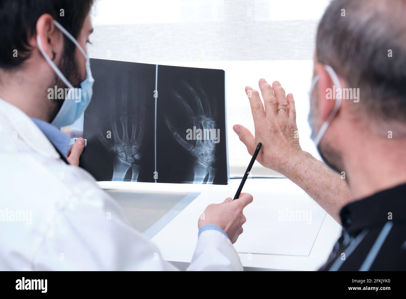 Young doctor examining xray of hands of a senior patient with