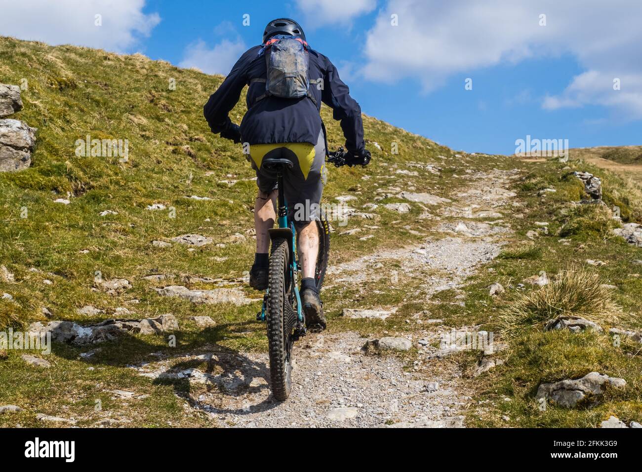 Mountain biker ascends steep bridleway from Halton Gill in the Yorkshire Dales heading towards Yockenthwaite in Wharfedale wearing black and yellow cl Stock Photo