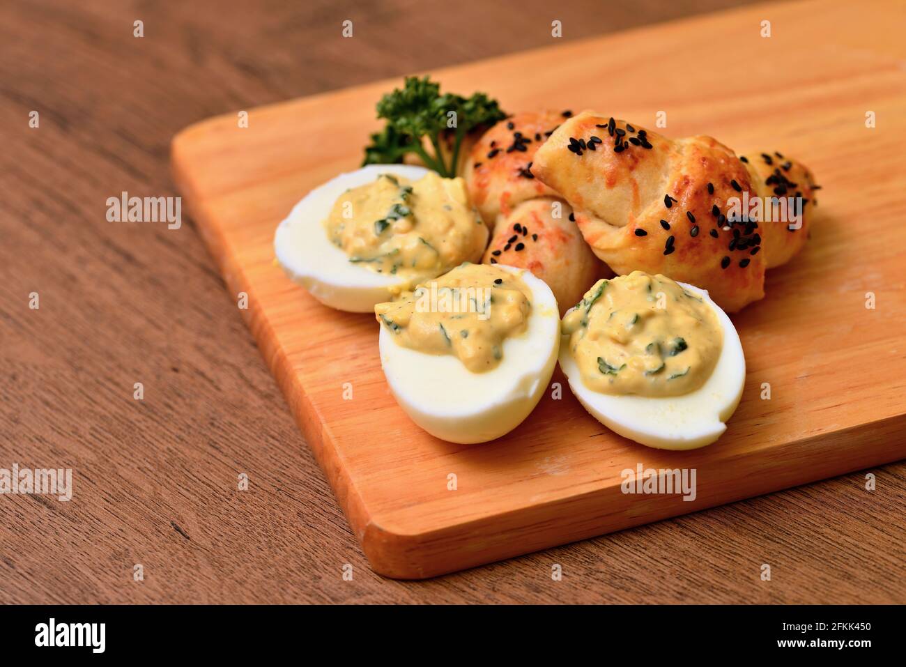 Eggs mimosa cheese mini-croissant on a wooden board. Arranged eggs and pastries with a sprig of curly parsley. Eggs stuffed with cream, homemade pastr Stock Photo