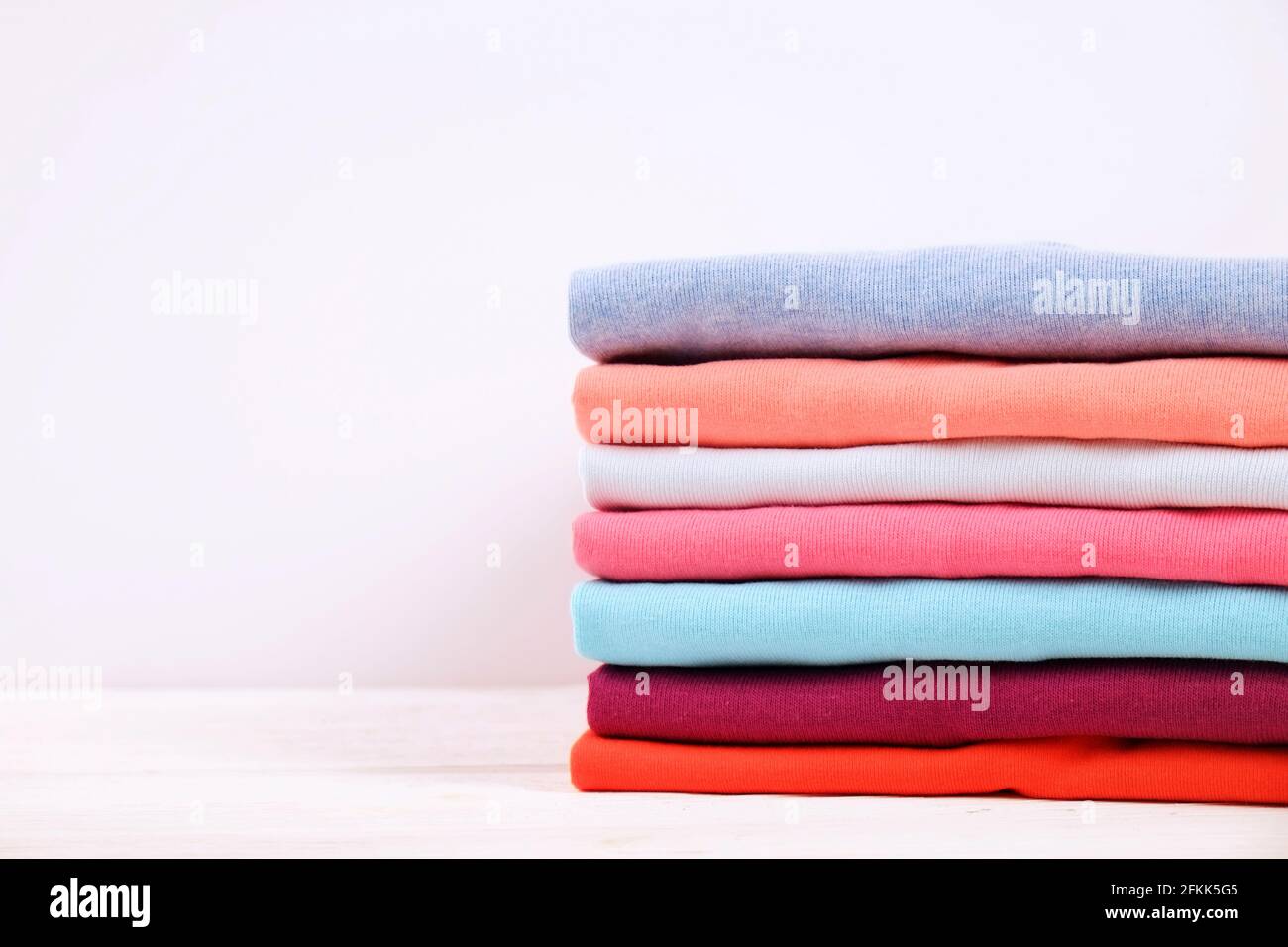 Stack of colorful perfectly folded tshirts on white wooden texture