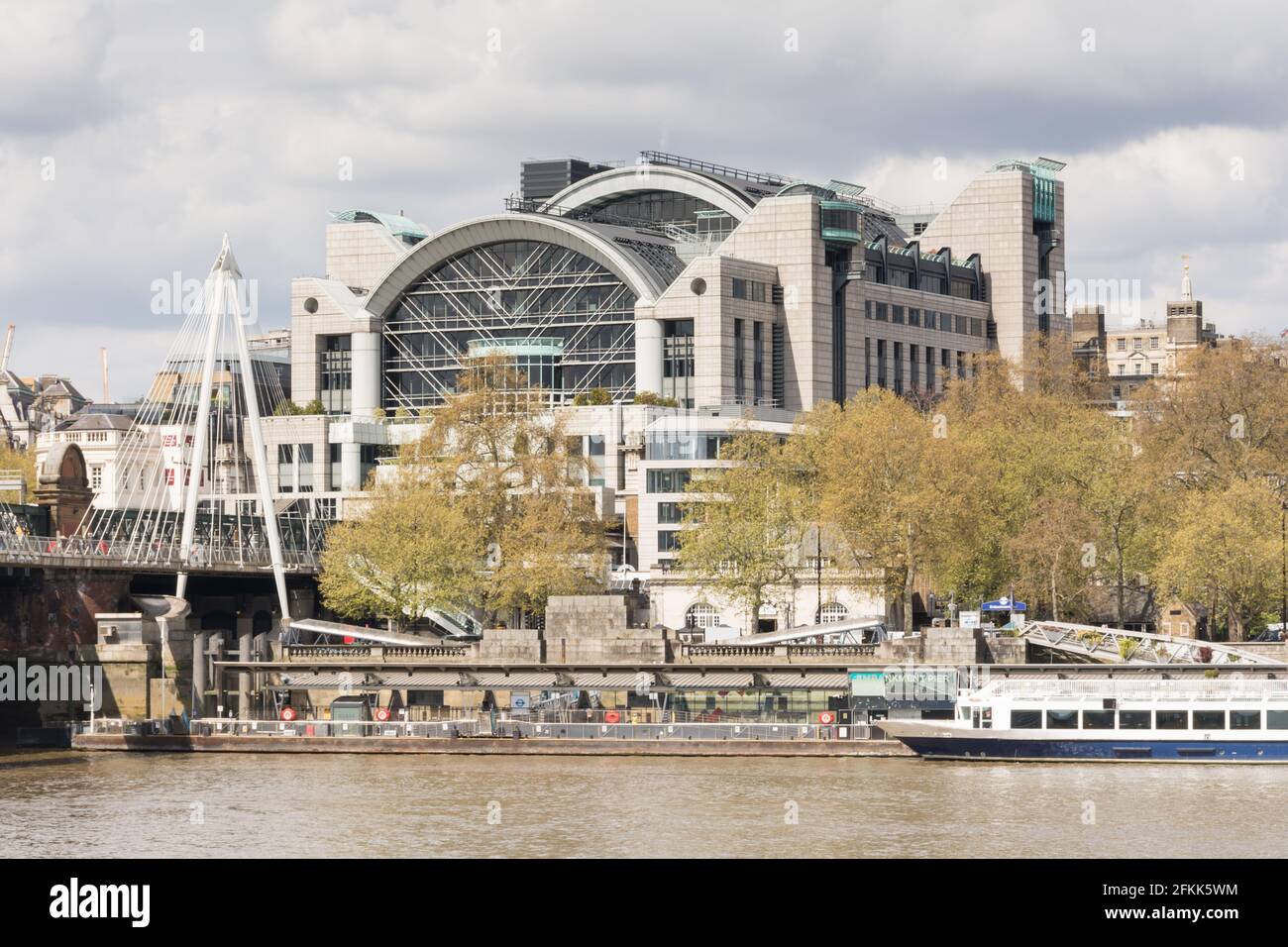 A sunlit Charing Cross station, on the Victoria Embankment, with the Embankment landing stage on the River Thames in the foreground. Stock Photo