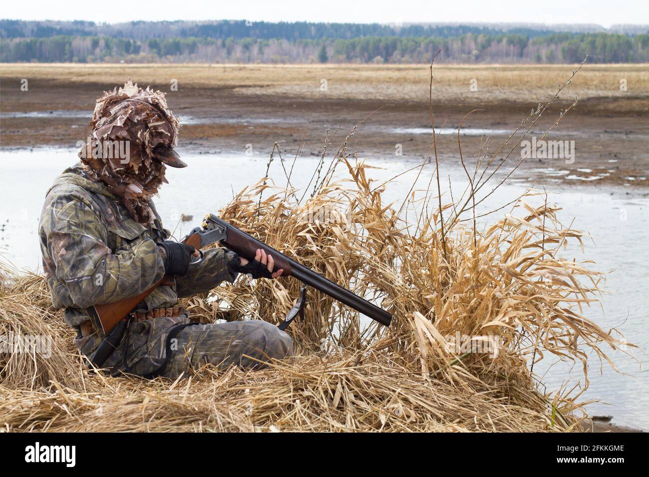 duck hunter charges his shotgun next to the hunting blind of reeds on the lake Stock Photo
