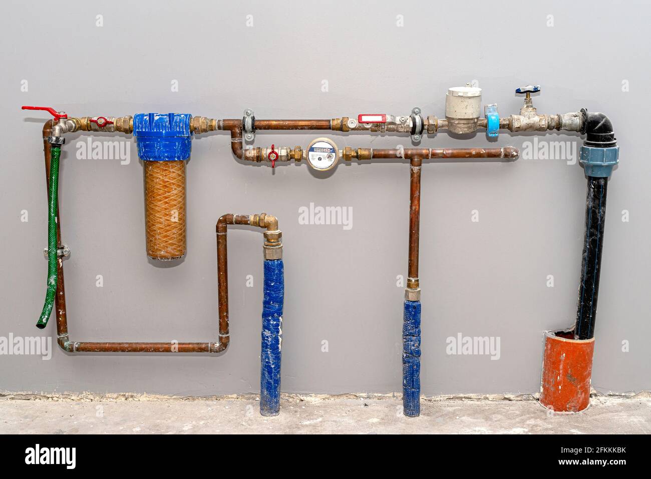 Two pipes with cold water flowing from the floor and a valve from the main water supply, domestic plumbing, visible copper pipes and a meter. Stock Photo