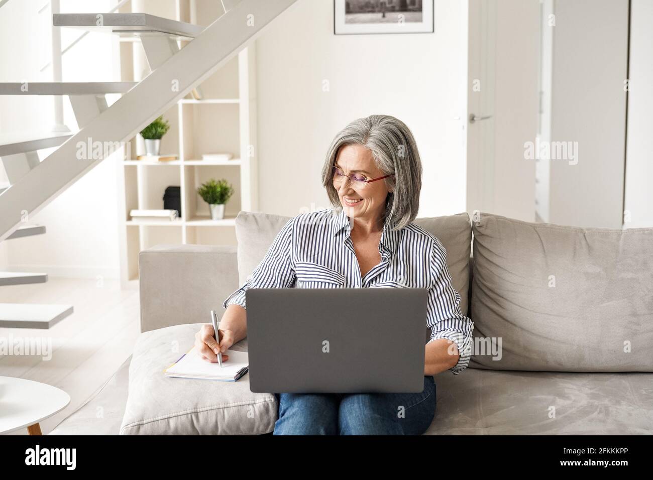 Happy mature old professional woman working on laptop from home office. Stock Photo