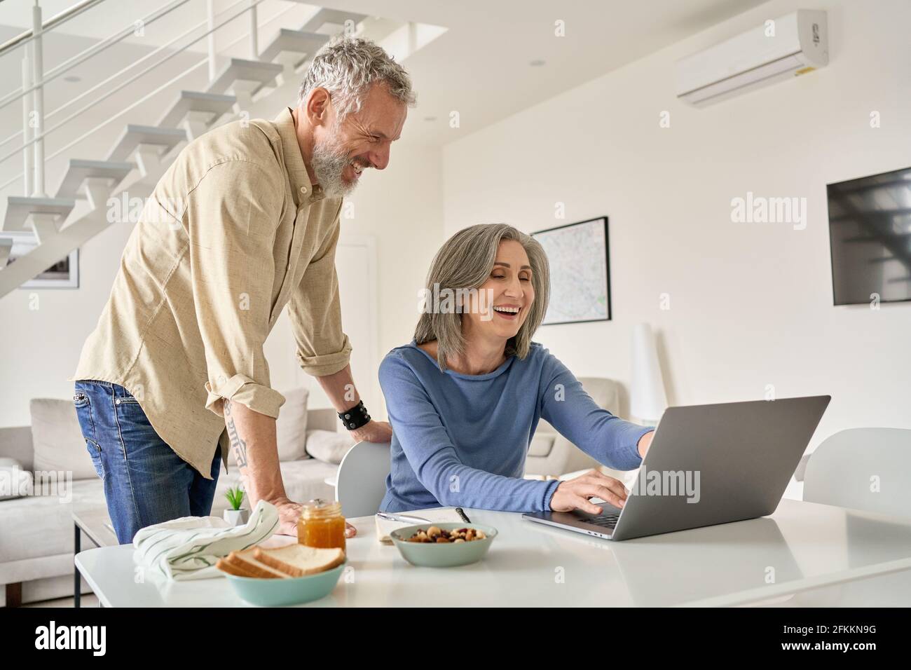 Happy middle aged couple having fun using laptop computer at home. Stock Photo