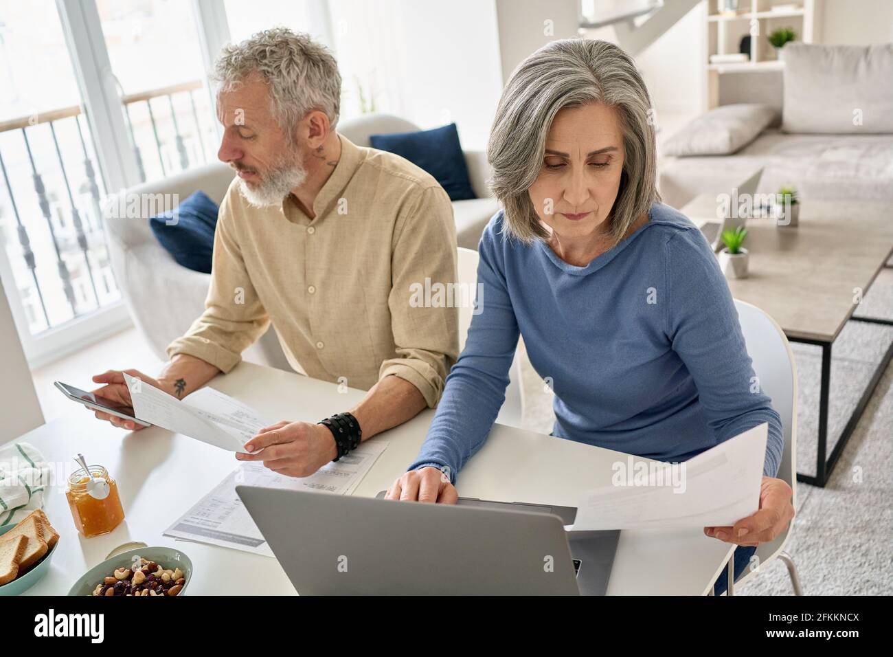 Mature couple reading documents bills paying bank loan using laptop and phone. Stock Photo