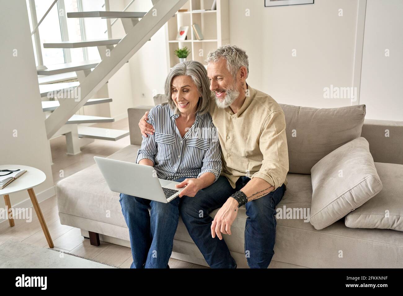 Happy old mid age family couple using laptop computer sitting on couch. Stock Photo