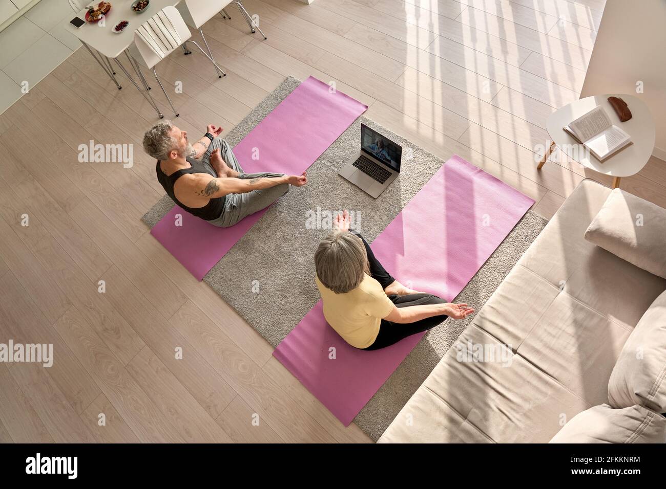 Old couple doing virtual yoga class meditating together at home, top view. Stock Photo