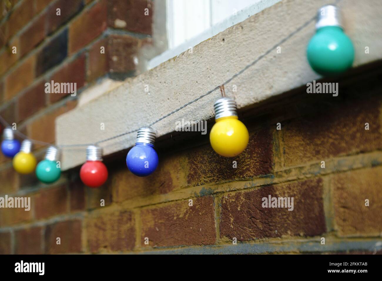 Coloured light bulbs hanging beneath a window sill. Stock Photo