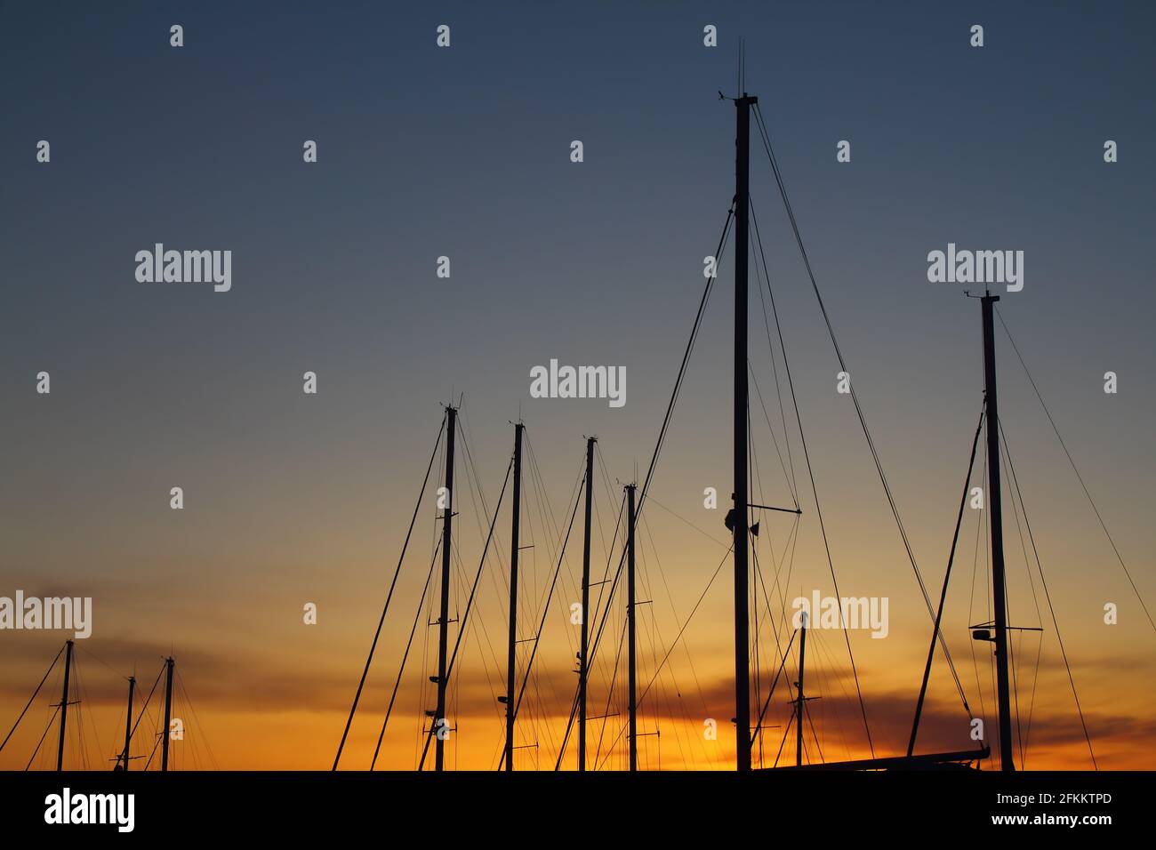 Fiery contrasting clouds in the blue sky, at sunset, through the masts of sailing yachts. Stock Photo