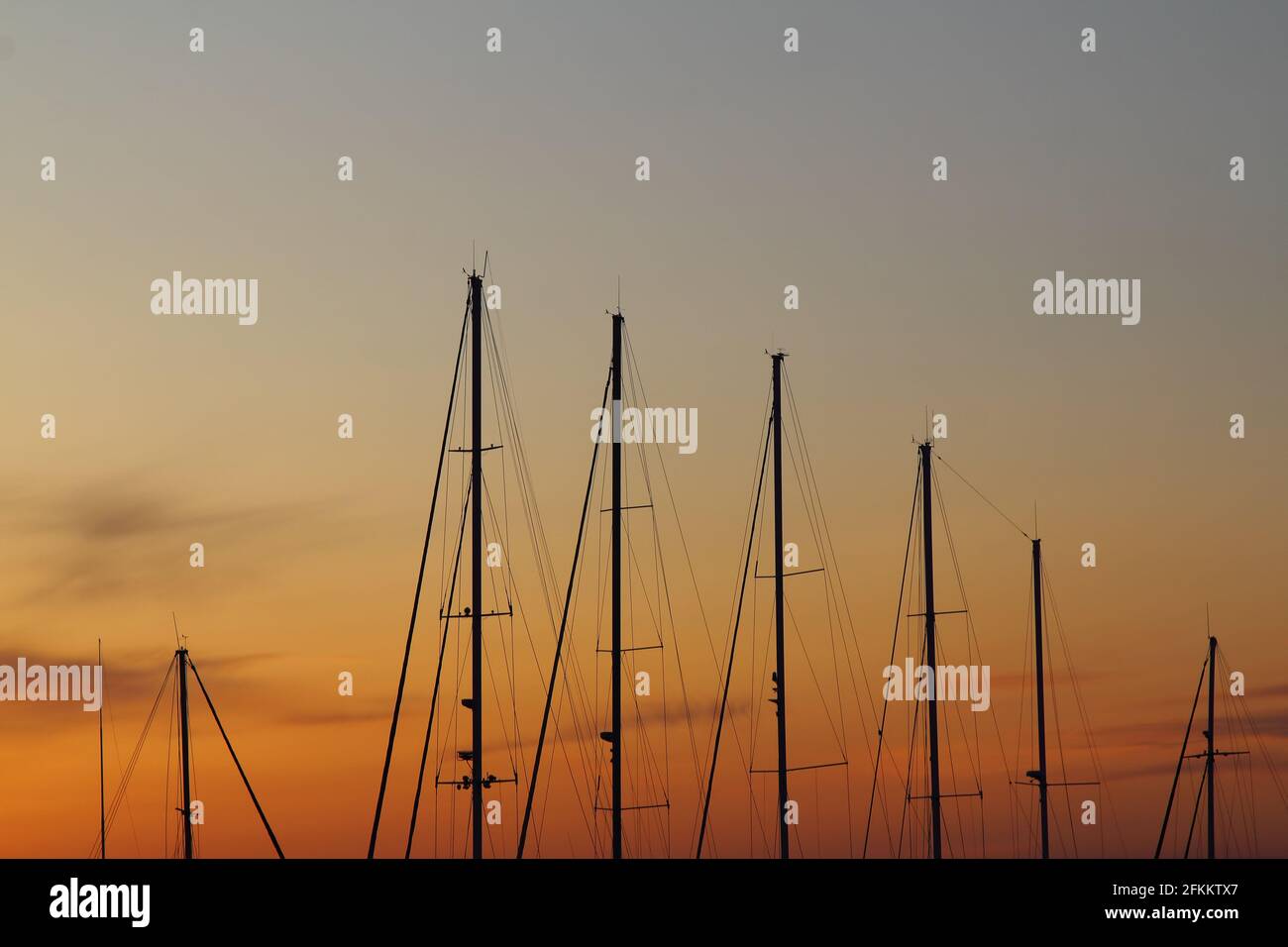 Fiery contrasting clouds in the blue sky, at sunset, through the masts of sailing yachts. Stock Photo