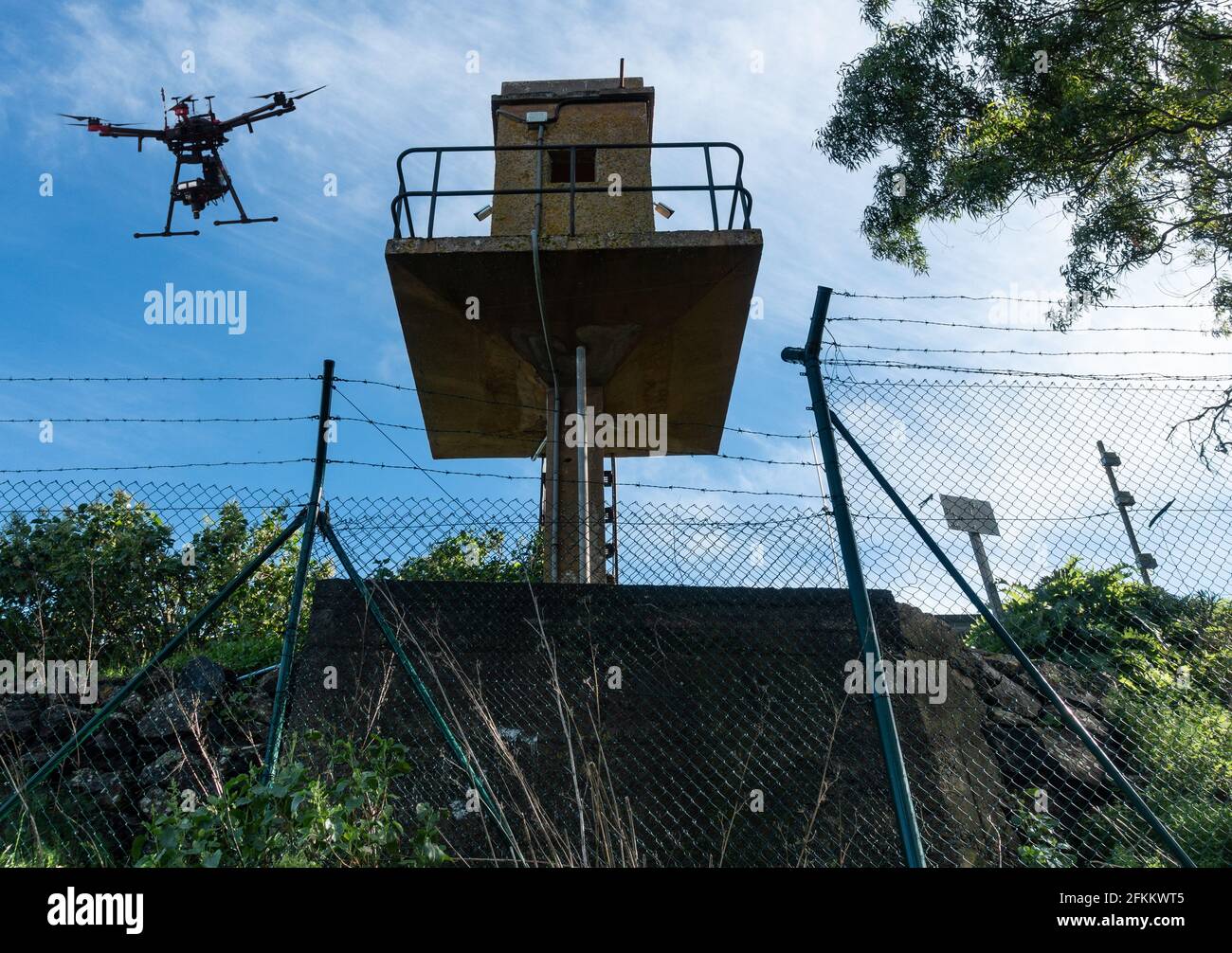 Drone flying above watchtower behind security, razor wire, barbed wire fence. Stock Photo