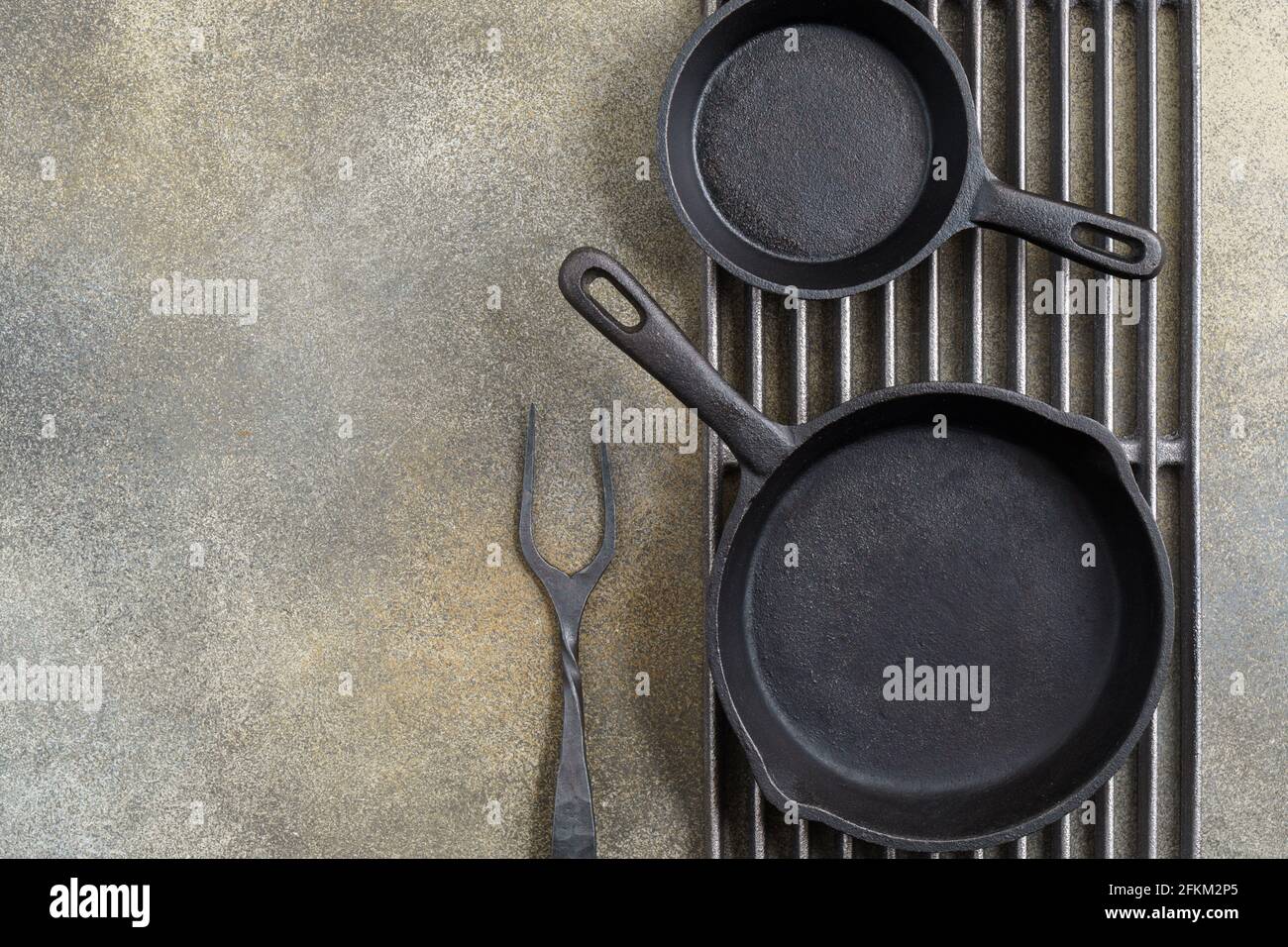 Grill grate with cast iron pans and fork on brown background with copy