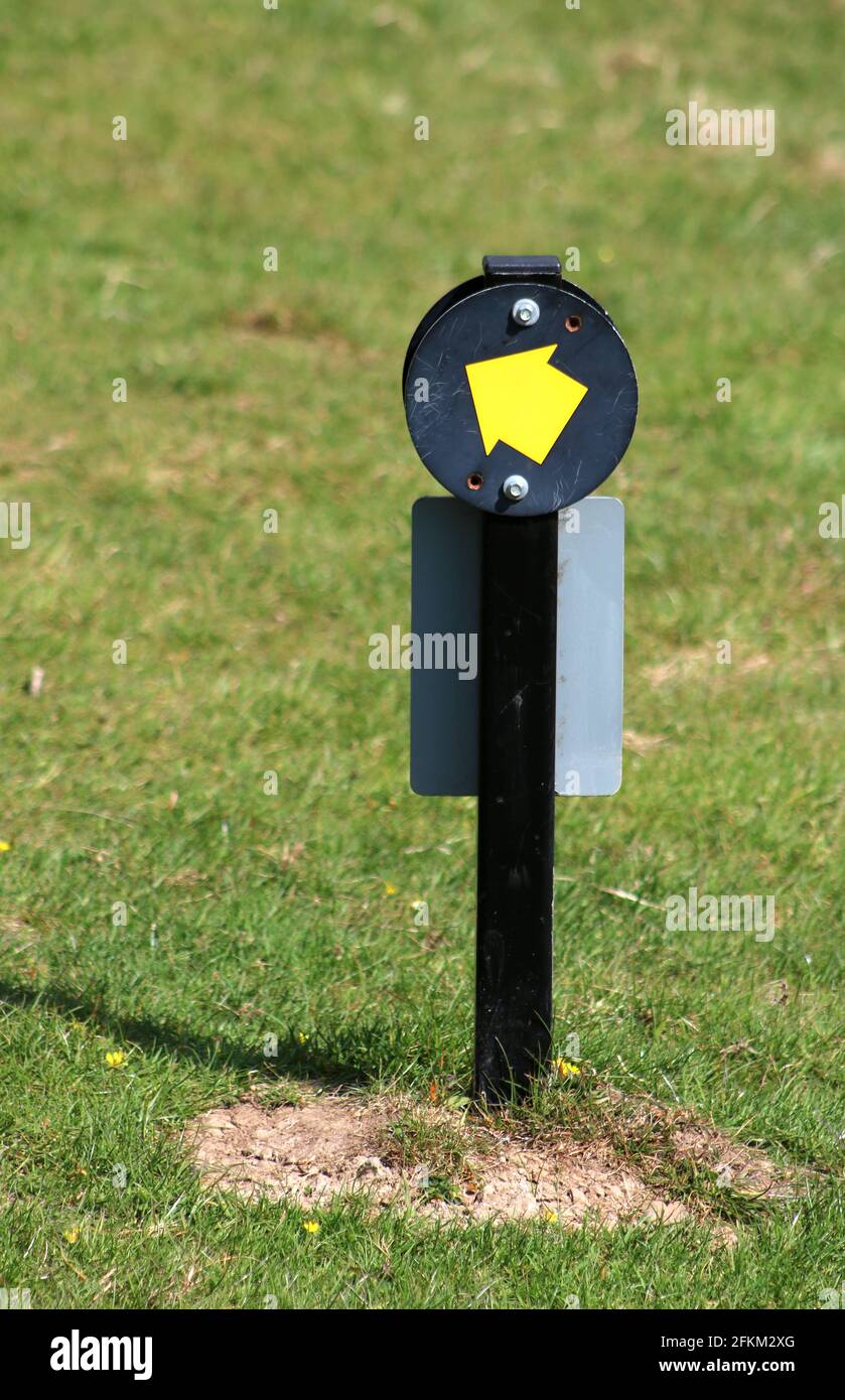 Disc with yellow arrow on black background on post indicating the direction taken by a public footpath through Levens Hall Deer Park at Levens. Stock Photo