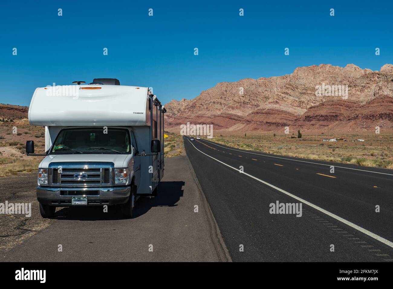 C-type camper with slideouts standing in the desert on the side of the road with mountains in the background and a highway passing Stock Photo