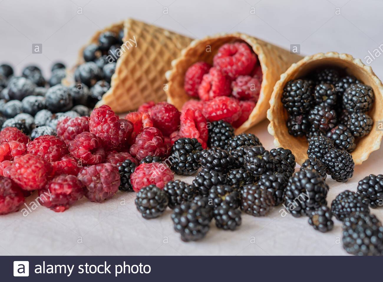 Three waffle cones close-up of which poured on the table raspberries, currants, blackberries in powdered sugar Stock Photo