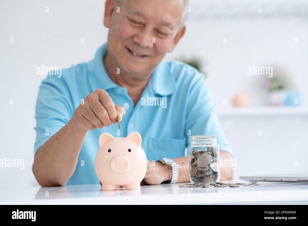 Elder man smiling putting a coin inside piggy bank Stock Photo - Alamy