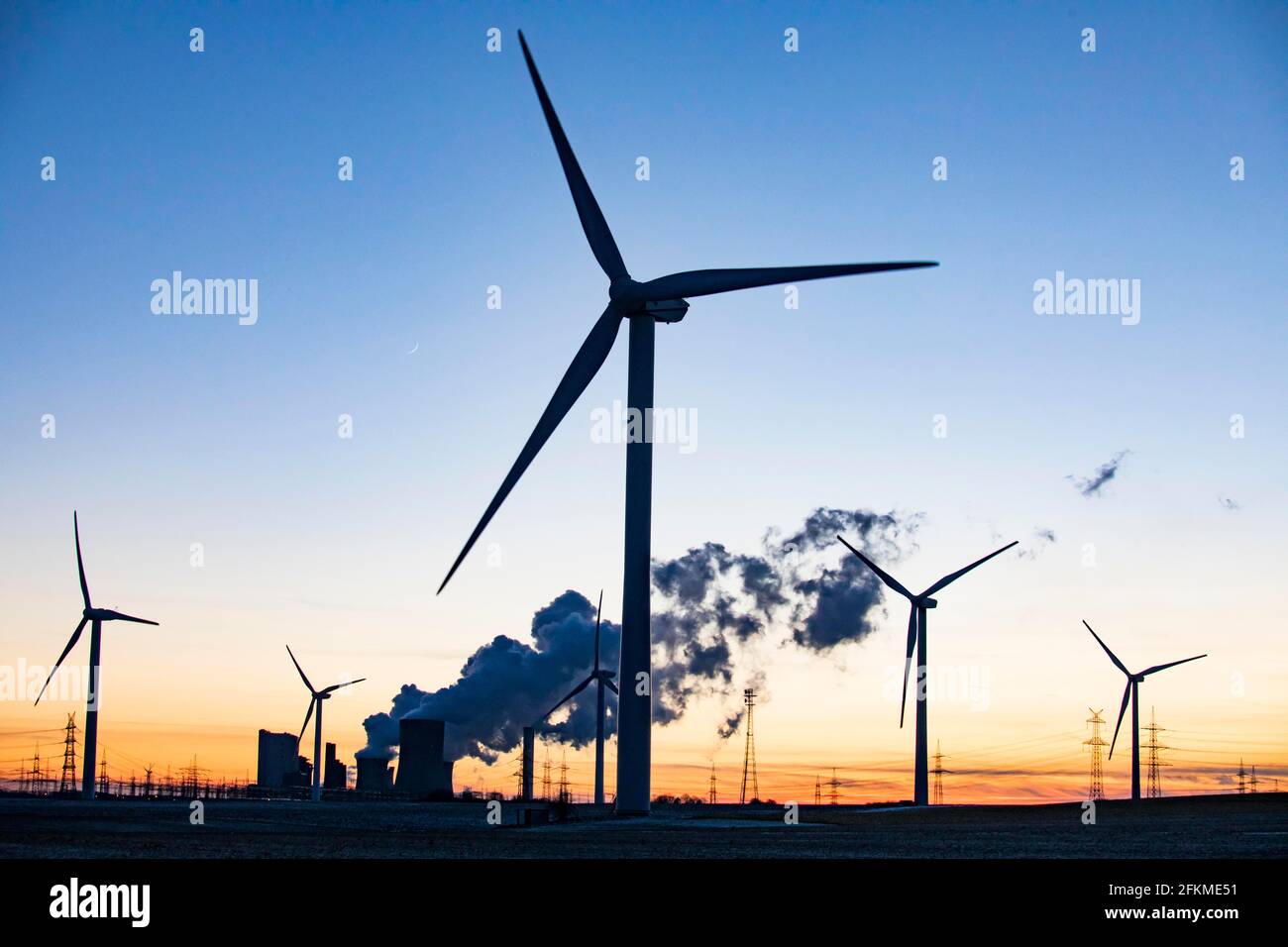 Wind turbines in front of steaming coalfired power plant at sunset