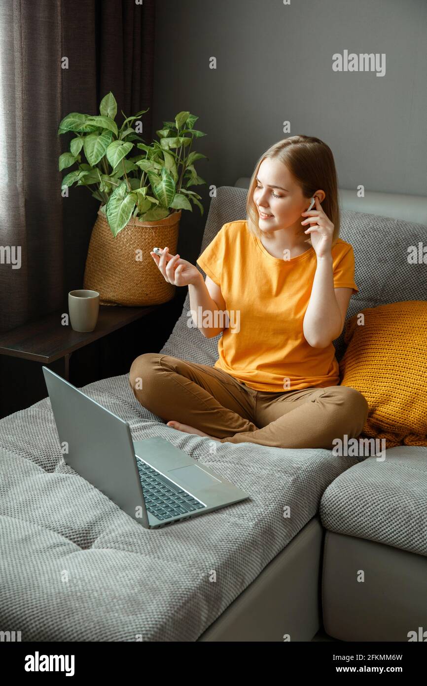 Pensive Caucasian beautiful woman work using laptop headphones remotely from home. Portrait of teenage girl student thinking at home in living room Stock Photo