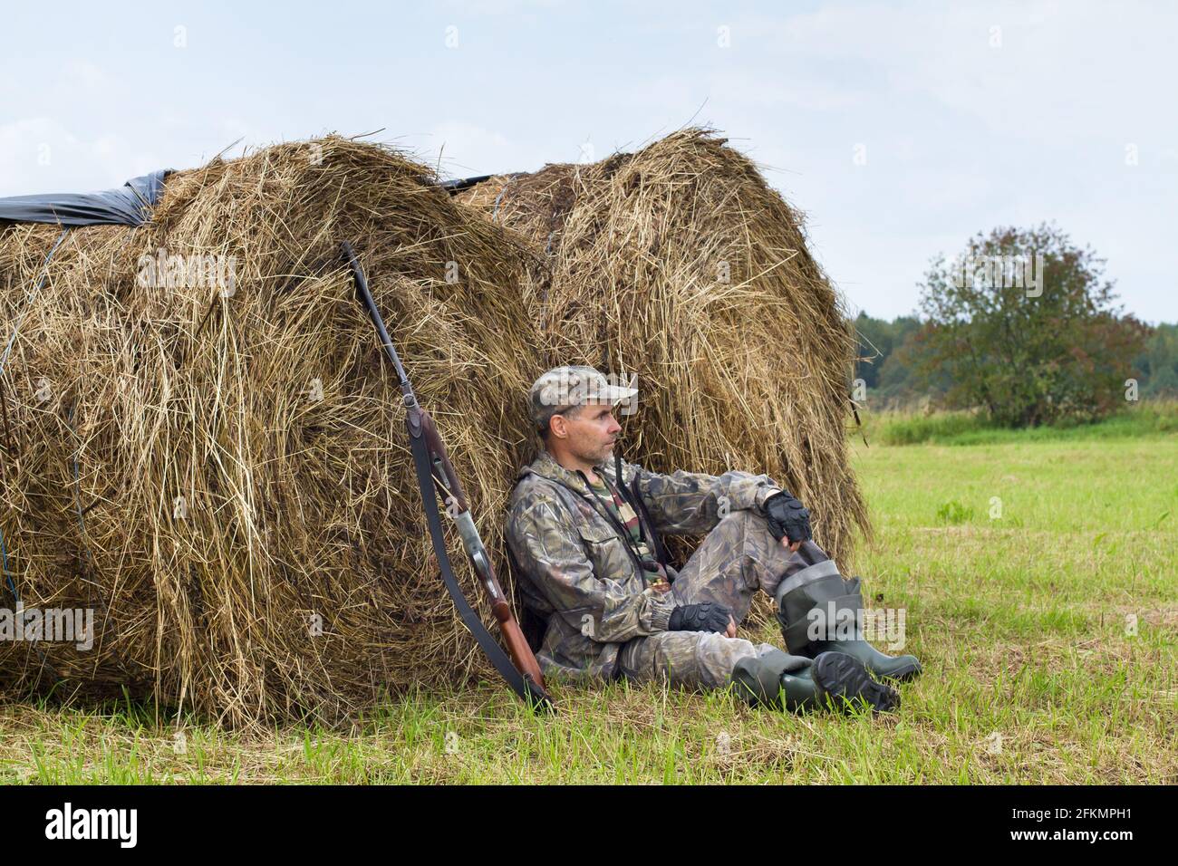 hunter with his shotgun resting on the hayfield during the autumn hunting Stock Photo