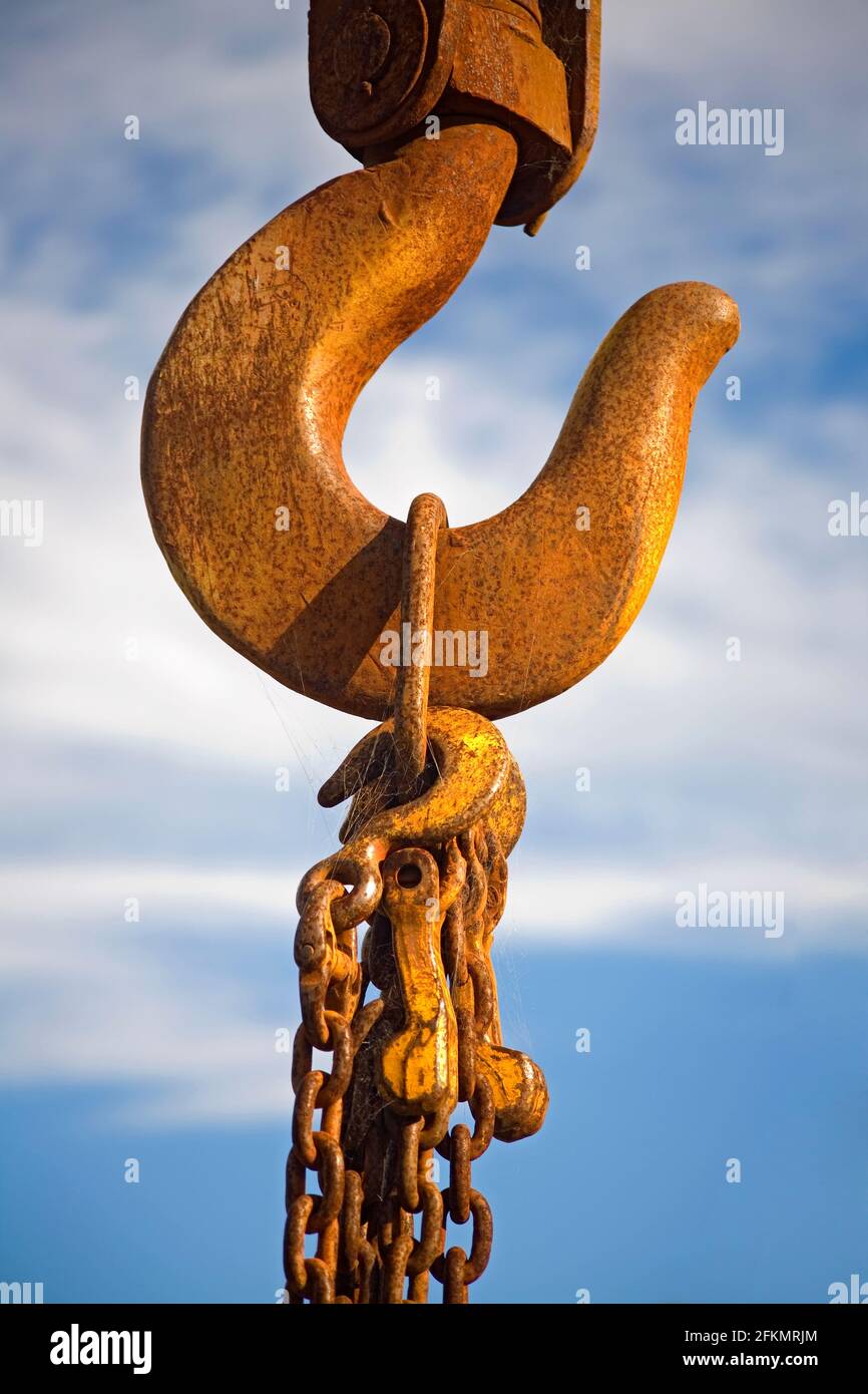 Rusty old crane hook with chains hanging on it. Blue sky background